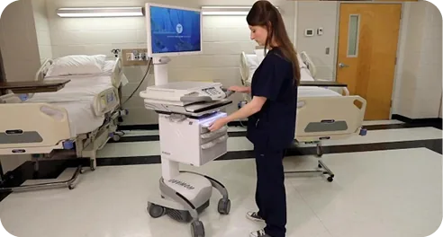 Nurse using a hospital-grade medical computer cart beside patient beds